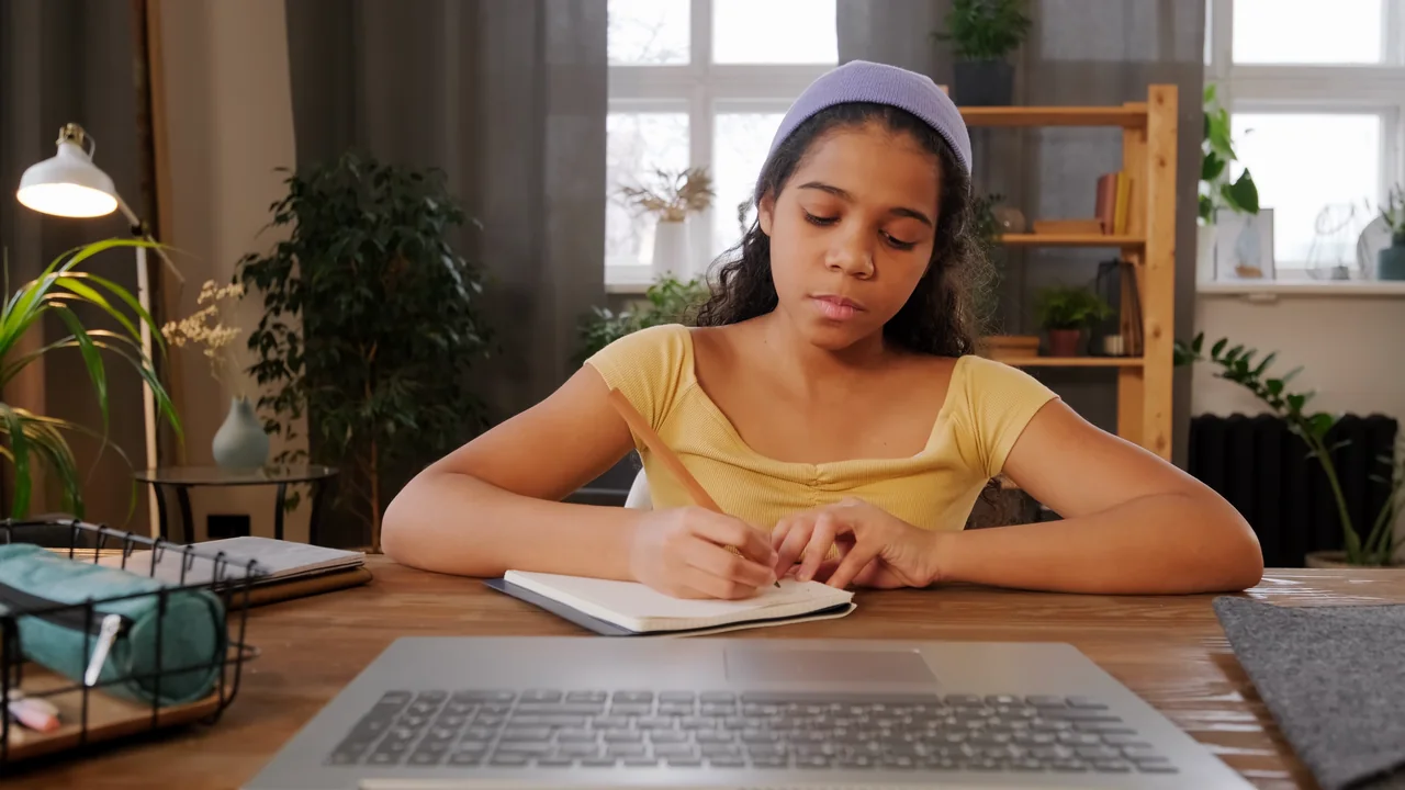 A girl taking notes during an online class at home